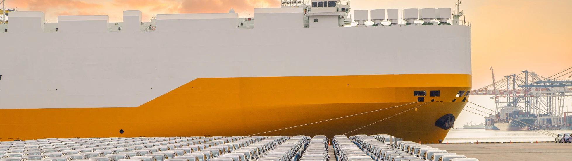 new cars parked in front of a ship in the harbour